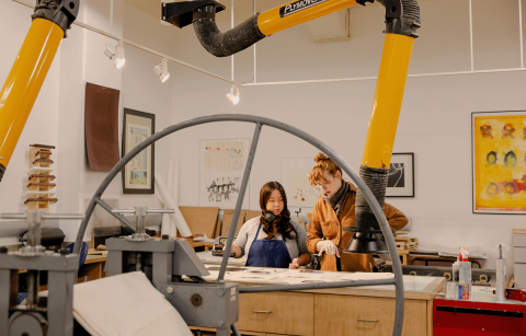Instructor and student looking at prints on a table in a printmaking studio class