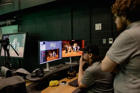 Students work on a computer in a green screen room.