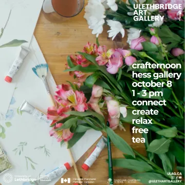 paint tubes, botanical sketches, fan brush with blue paint on the tips, glass with liquid, and various flowers, all on a wood table.