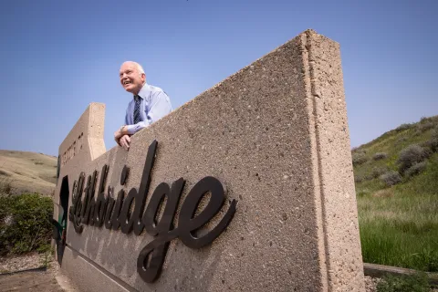 Dennis Connolly leaning over the welcome to Lethbridge concrete sign, looking off into the distance and smiling