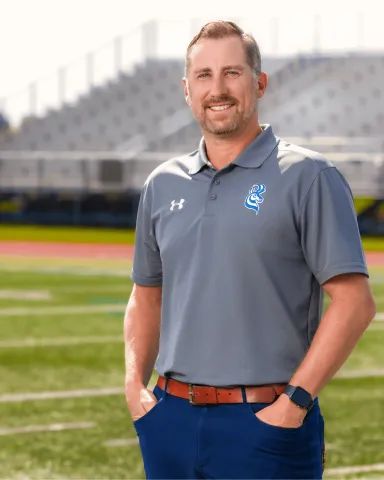 Darryl Moore (BMgt ’02) stands on a sports field at ULethbridge