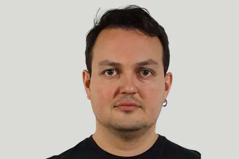 man with an earring in a black shirt in front of a plain wall