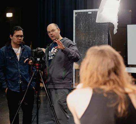 A professor is explaining camera work to a student in an Acting for the Camera course with the subject blurred in the foreground.
