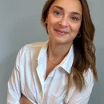 Picture of Elizabeth Cavaliere from the waist up; she has long brown hair and is wearing a white shirt.