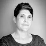 A black and white photograph of Mary-Ann McTrowe from the shoulders up.  She has short, dark hair, white skin, and is smiling.