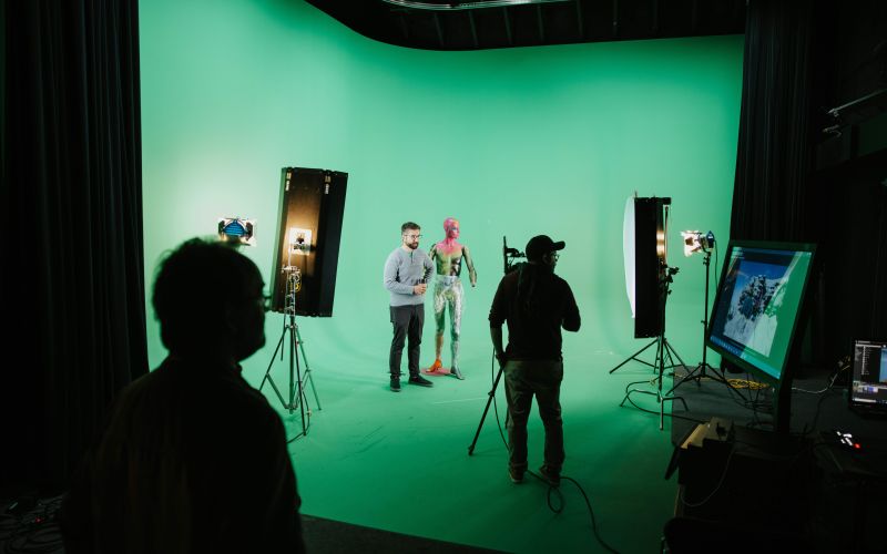 People setting up cameras and lights in a green screen room.