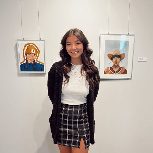 photo of Kiyomi Scoville standing in front of two illustrative artworks.